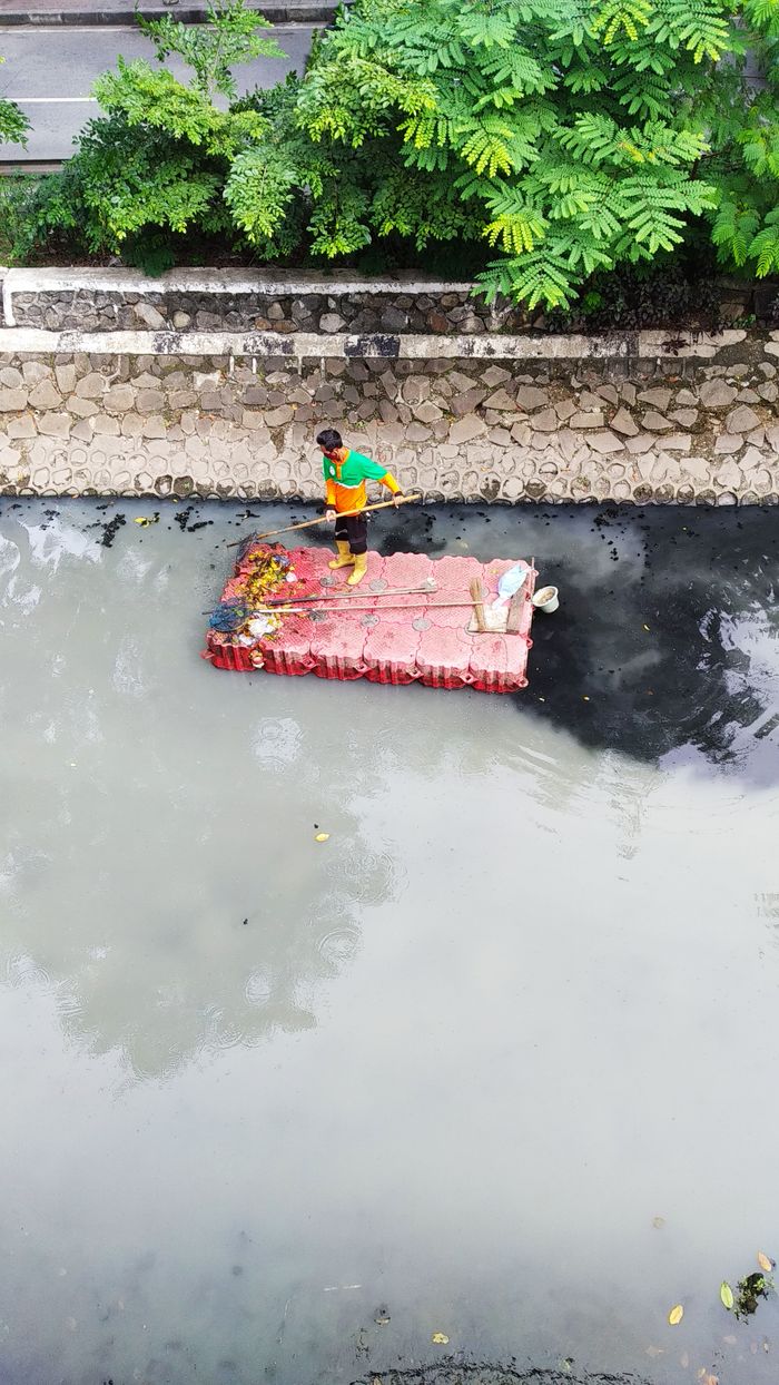 why-choose-us Man standing on raft cleaning a polluted river from above. Aerial perspective.